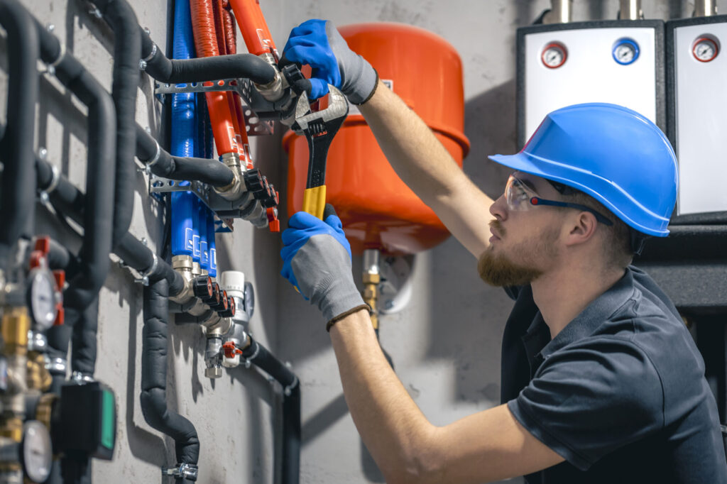 a man installs a heating system in a house and checks the pipes with a wrench.