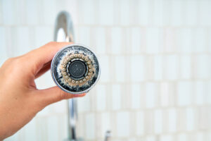 a woman is holding a chrome faucet covered with lime scale.